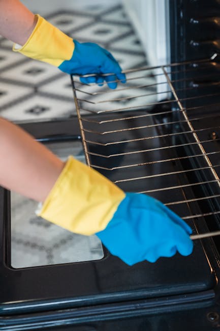 A worker from Oven Cleaning Bow is engaged in a commercial surface cleaning process outdoors on a city street. The worker is wearing a high-visibility safety vest and gloves, operating a portable pres